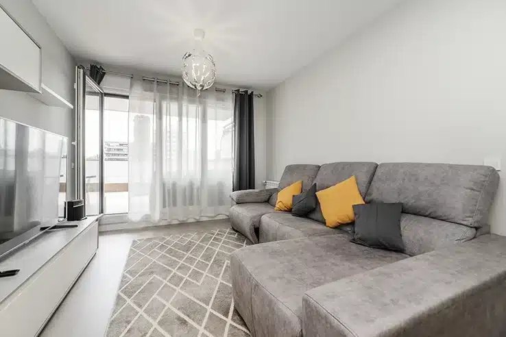 Las pequeñas decisiones que hacen que una vivienda parezca mucho más amplia Salón pequeño con sofá gris y distribución para aprovechar el espacio.